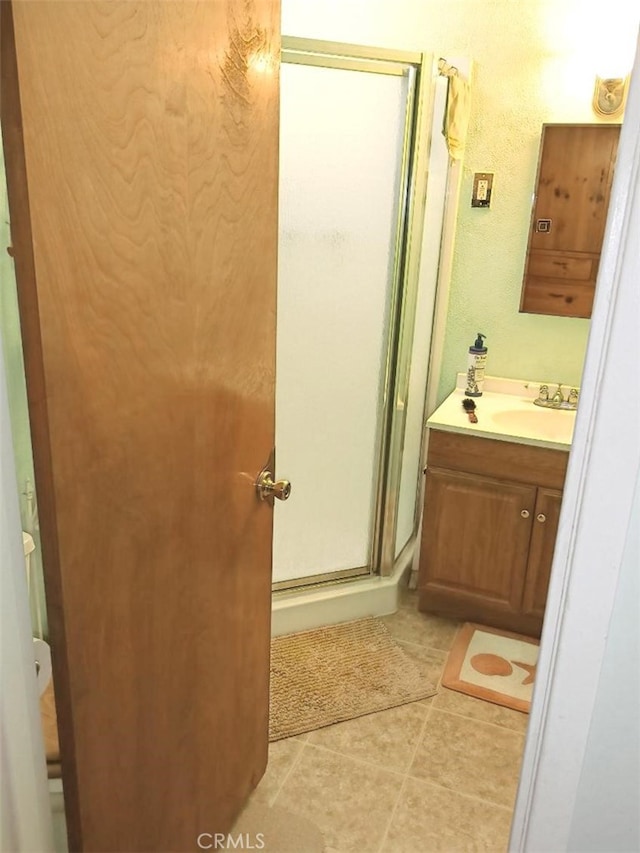 bathroom with tile patterned floors, a shower stall, vanity, and a textured wall