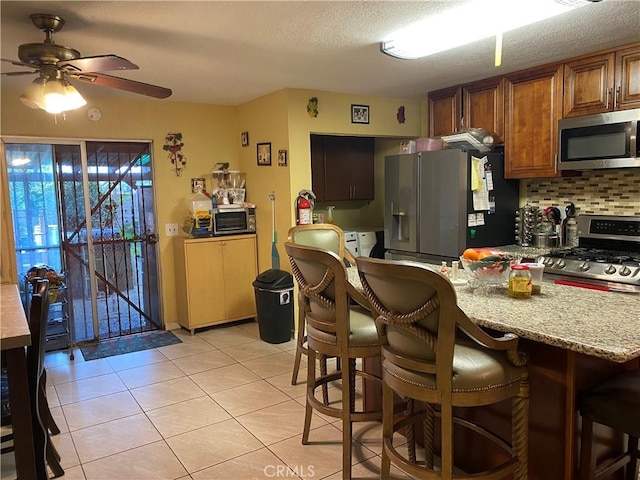 698 W Phillips Blvd, Pomona, CA 91766 - kitchen with decorative backsplash, ceiling fan, stainless steel appliances, brown cabinetry, and light tile patterned floors