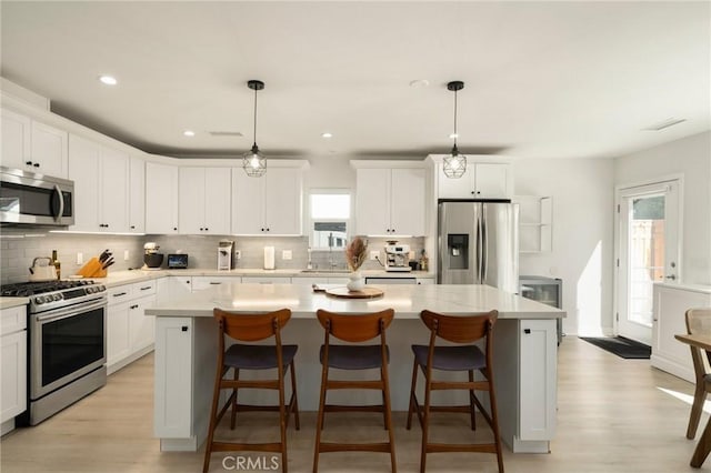 kitchen featuring light wood-style floors, tasteful backsplash, appliances with stainless steel finishes, and a kitchen island