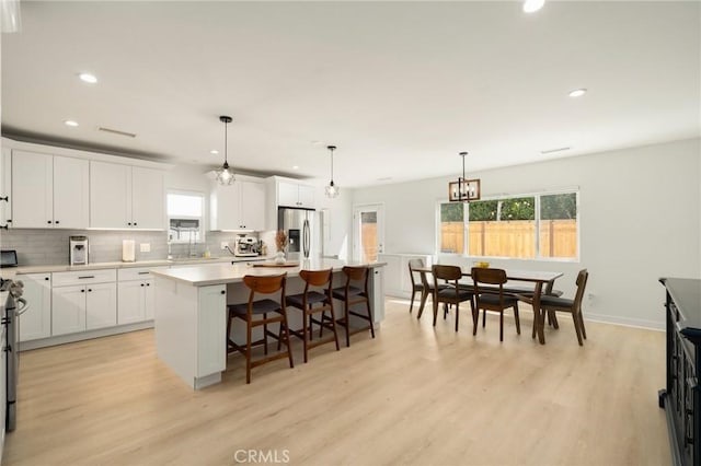 kitchen featuring a center island, stainless steel fridge, tasteful backsplash, recessed lighting, and light wood-style floors