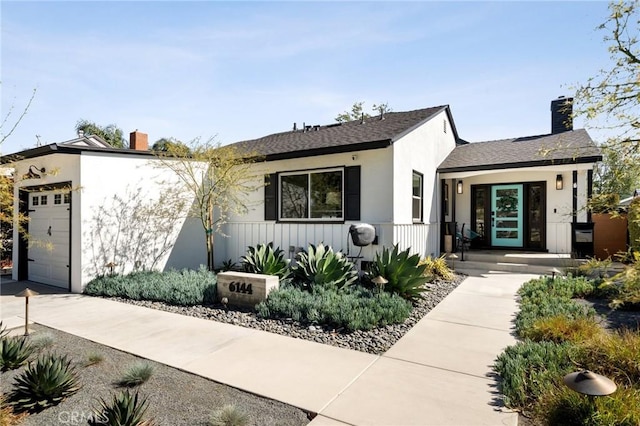 view of front of property featuring driveway, a garage, stucco siding, and a chimney