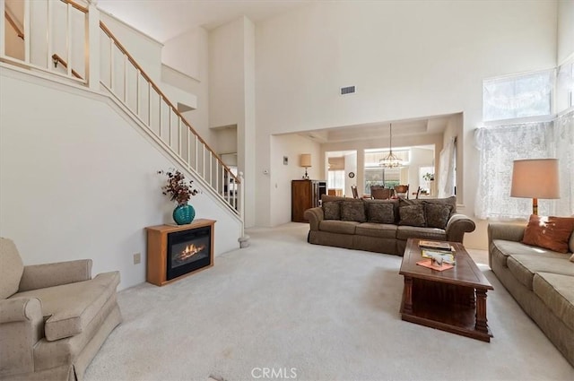carpeted living area with a notable chandelier, visible vents, a high ceiling, and stairway