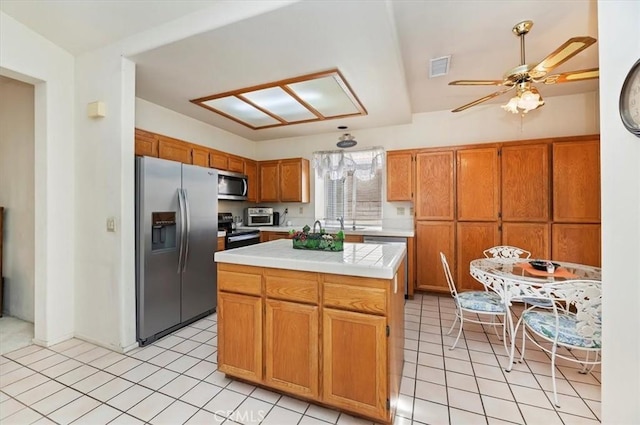 kitchen featuring stainless steel appliances, brown cabinets, tile countertops, visible vents, and a ceiling fan