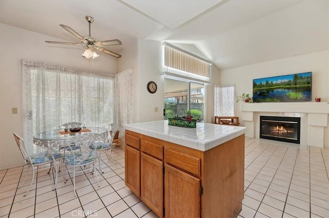 kitchen featuring a ceiling fan, light tile patterned floors, a glass covered fireplace, vaulted ceiling, and tile counters