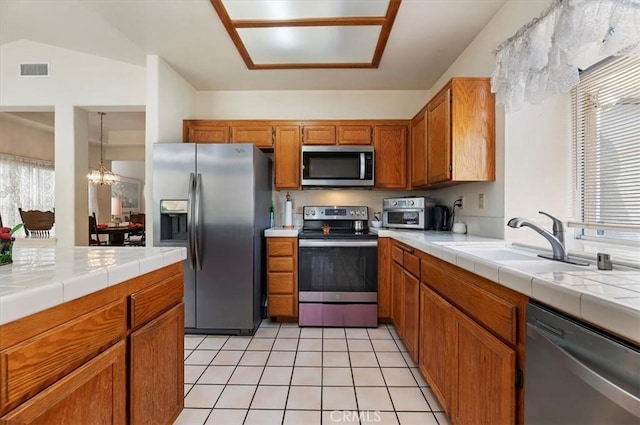 kitchen with brown cabinets, stainless steel appliances, tile countertops, and a sink
