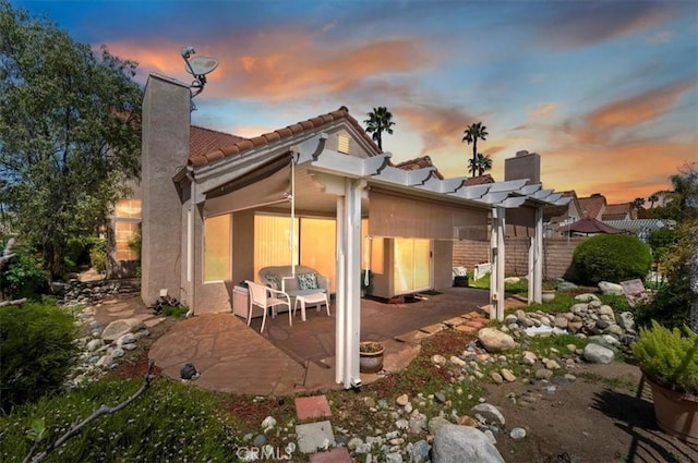back of house with a chimney, a patio area, a pergola, and a tiled roof