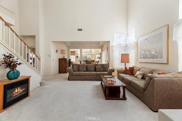 living area featuring visible vents, stairway, a chandelier, carpet floors, and a high ceiling
