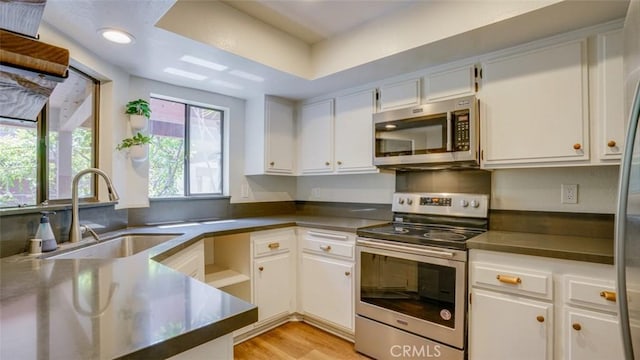 kitchen featuring dark countertops, light wood-type flooring, white cabinetry, a sink, and appliances with stainless steel finishes