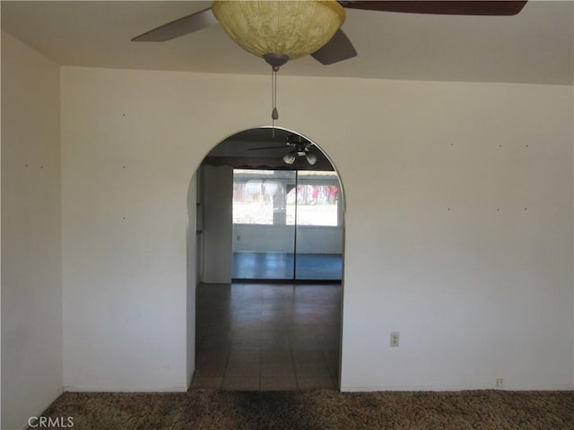 tiled spare room with arched walkways, carpet, and a ceiling fan