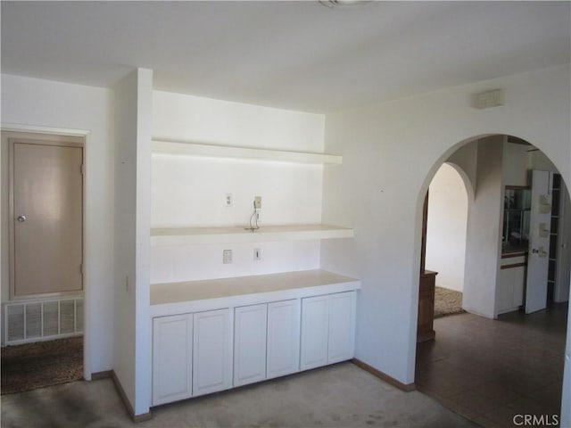 kitchen with light countertops, visible vents, baseboards, arched walkways, and open shelves