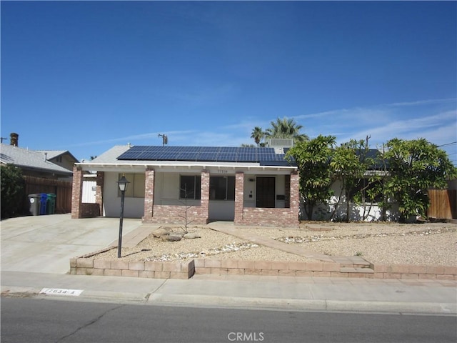 view of front of house with brick siding, fence, and roof mounted solar panels