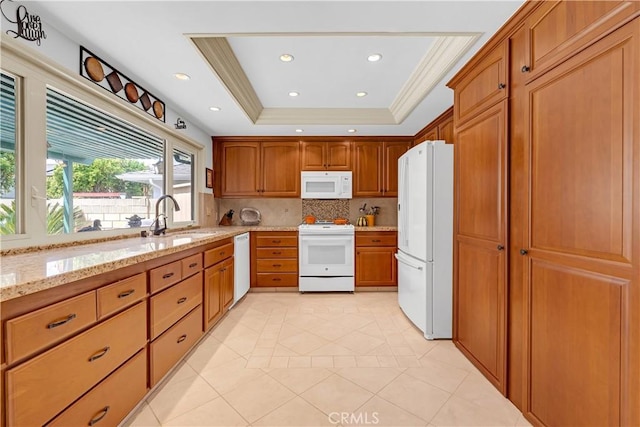 kitchen featuring tasteful backsplash, light stone counters, white appliances, brown cabinetry, and a sink