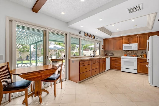 kitchen with white appliances, visible vents, brown cabinets, and a raised ceiling