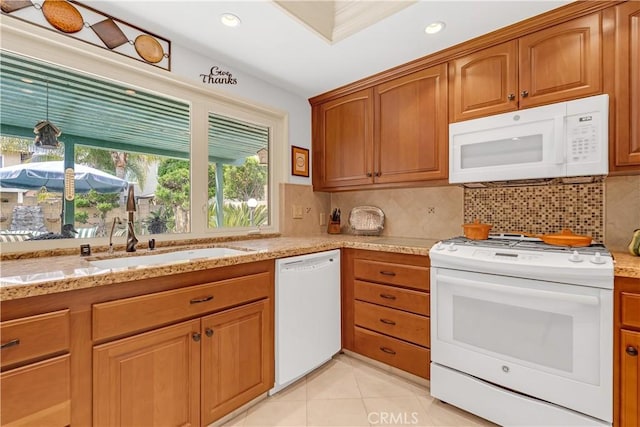 kitchen with white appliances, light stone countertops, brown cabinetry, decorative backsplash, and a sink