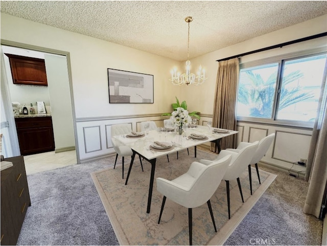 dining area with a chandelier, a textured ceiling, a wainscoted wall, a decorative wall, and light colored carpet