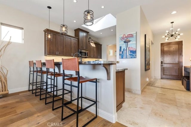 2865 Rock Wren Ln, Avila Beach, CA 93424 - kitchen with stainless steel microwave, a chandelier, light stone countertops, a kitchen breakfast bar, and dark brown cabinetry