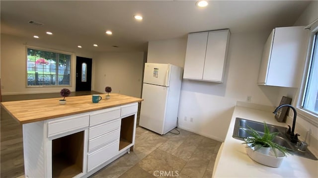 kitchen featuring recessed lighting, a sink, butcher block counters, freestanding refrigerator, and white cabinets