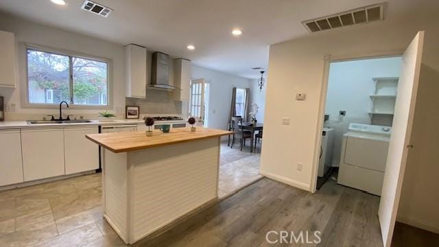 kitchen featuring wall chimney range hood, visible vents, butcher block countertops, and a sink
