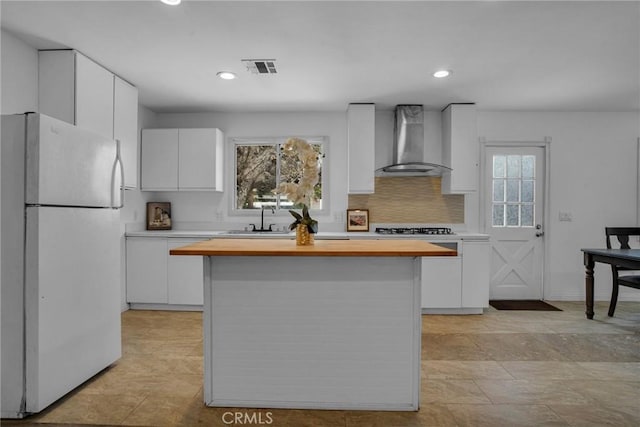 kitchen featuring butcher block countertops, white cabinets, a sink, wall chimney range hood, and freestanding refrigerator