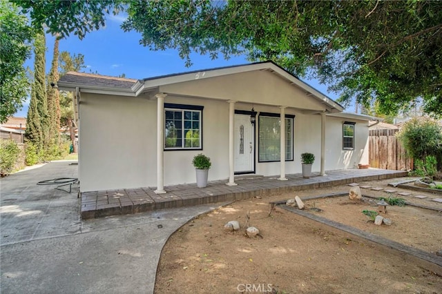 single story home featuring a porch, stucco siding, and fence