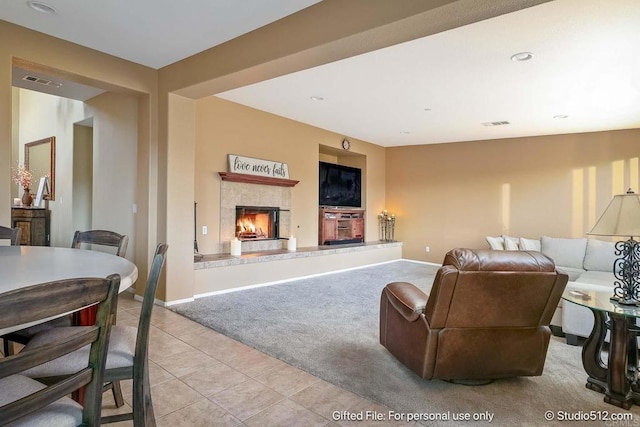 living room featuring light carpet, baseboards, visible vents, a lit fireplace, and light tile patterned floors