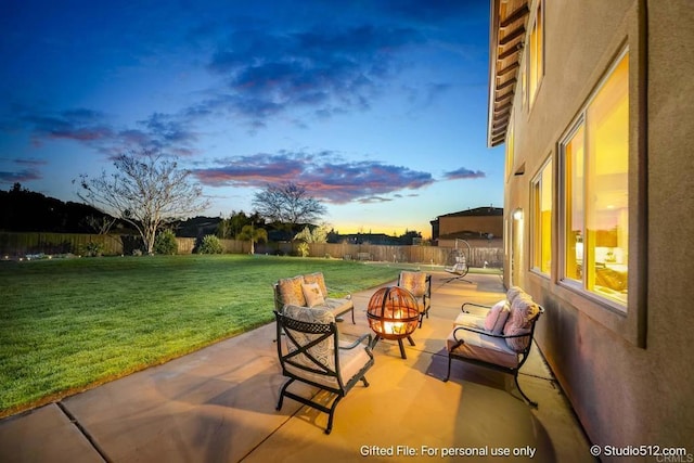 patio terrace at dusk with a fenced backyard, an outdoor fire pit, and a yard