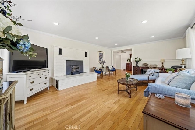 living room with ceiling fan, a brick fireplace, light wood-style floors, ornamental molding, and recessed lighting