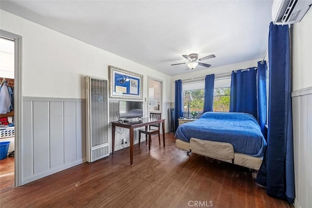 bedroom with an AC wall unit, a heating unit, wainscoting, and wood finished floors