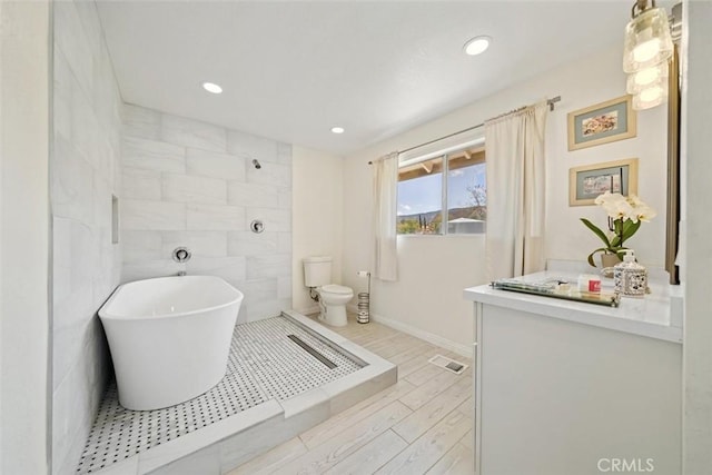 bathroom with wood finished floors, toilet, tile walls, recessed lighting, and a soaking tub