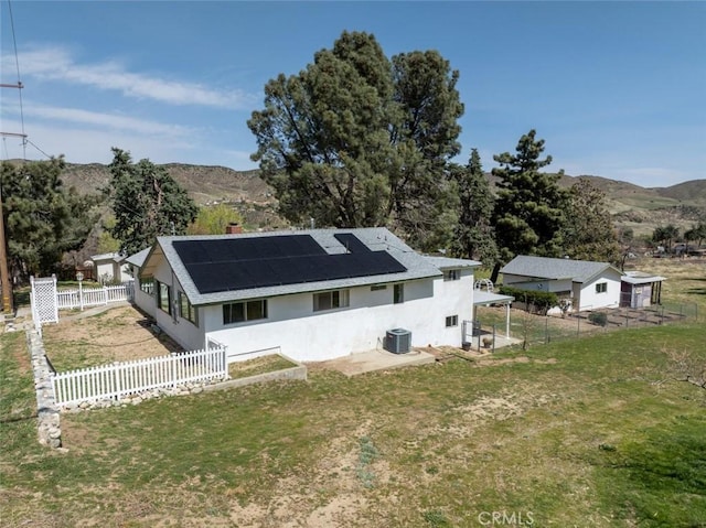 back of property with roof mounted solar panels, central AC unit, a mountain view, and a fenced backyard