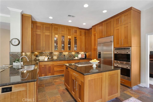 kitchen featuring dark stone counters, stainless steel appliances, a sink, backsplash, and stone tile floors
