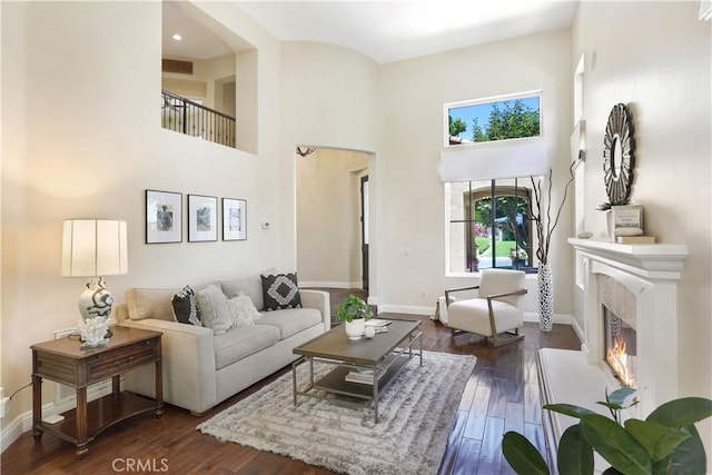 living area with baseboards, dark wood finished floors, a towering ceiling, visible vents, and a high end fireplace