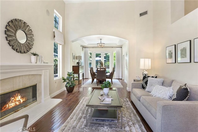 living room with baseboards, arched walkways, visible vents, a tiled fireplace, and wood finished floors