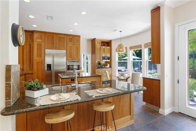 kitchen featuring dark stone countertops, a sink, a peninsula, appliances with stainless steel finishes, and brown cabinetry
