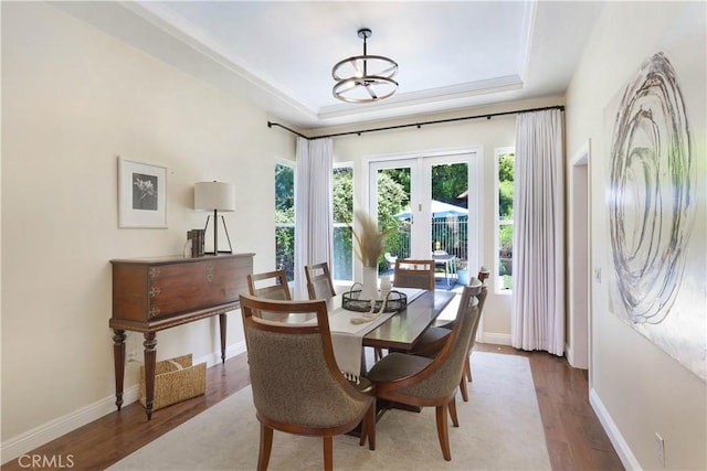 dining room featuring french doors, baseboards, a chandelier, a raised ceiling, and wood finished floors