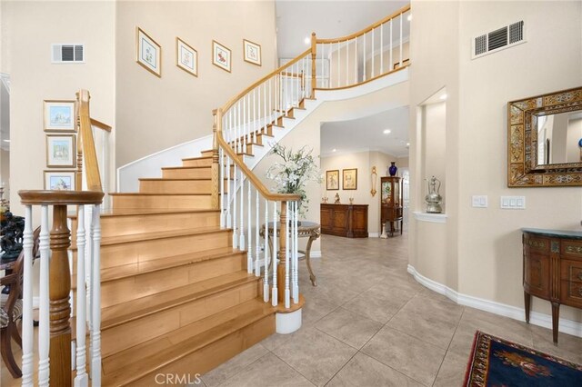 stairs with tile patterned flooring, a high ceiling, baseboards, and visible vents