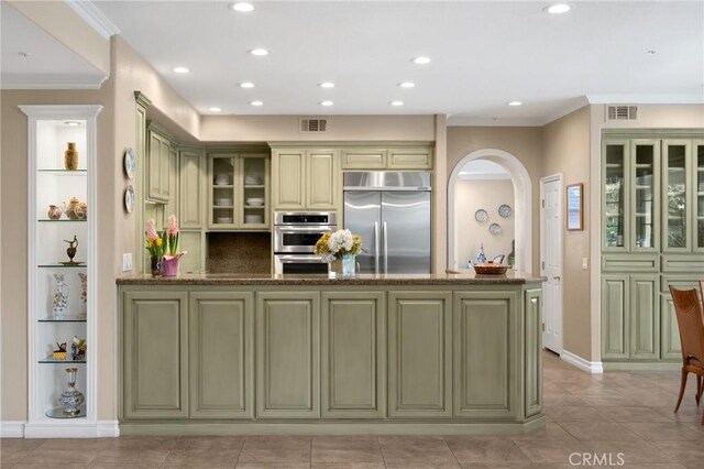 kitchen with arched walkways, built in shelves, green cabinets, a peninsula, and stainless steel appliances