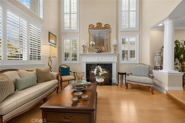 living area with decorative columns, a towering ceiling, wood finished floors, a fireplace, and baseboards
