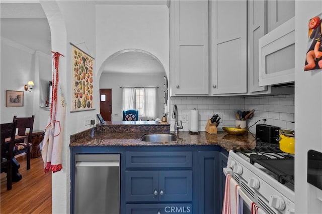 kitchen with backsplash, a sink, white appliances, arched walkways, and blue cabinetry