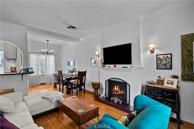 living area with visible vents, a chandelier, crown molding, wood finished floors, and a lit fireplace