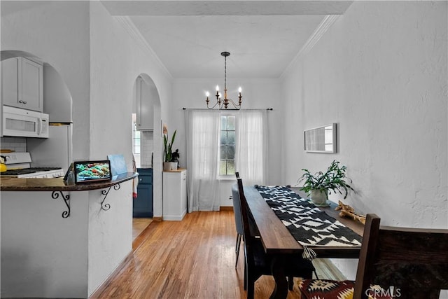 dining room featuring a chandelier, crown molding, light wood finished floors, arched walkways, and a textured wall