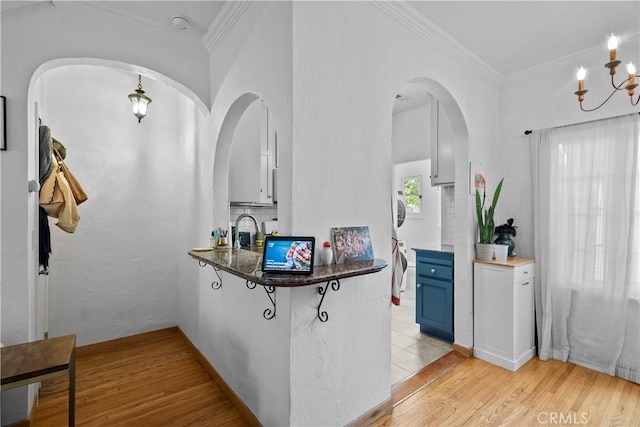 kitchen with blue cabinetry, ornamental molding, a chandelier, light wood-style flooring, and a peninsula