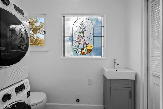 bathroom featuring baseboards, toilet, stacked washing maching and dryer, and vanity