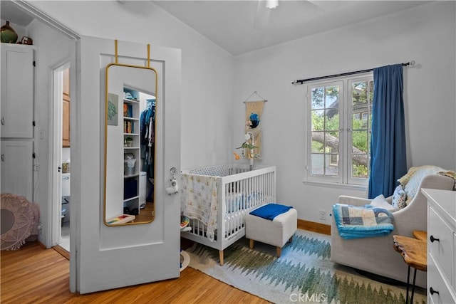 bedroom featuring a closet, light wood-style flooring, a crib, lofted ceiling, and a spacious closet