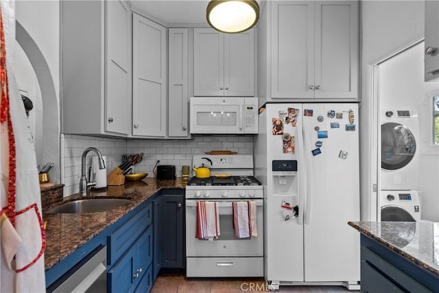 kitchen featuring stacked washer / dryer, a sink, tasteful backsplash, and white appliances