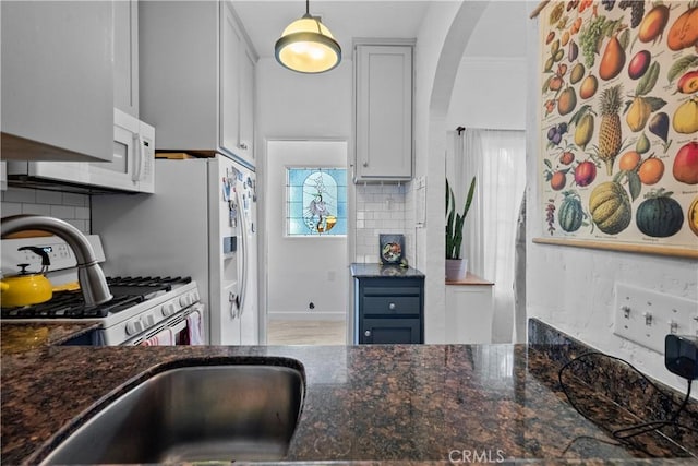 kitchen with white appliances, arched walkways, backsplash, and dark stone counters