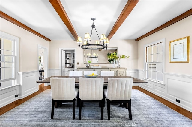 dining room with a healthy amount of sunlight, a wainscoted wall, dark wood-type flooring, and a chandelier
