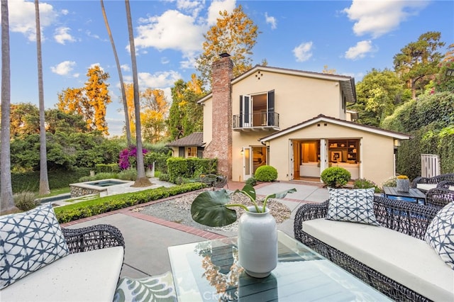 back of property featuring a hot tub, an outdoor hangout area, stucco siding, a balcony, and a patio