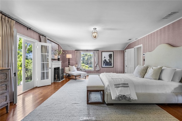 bedroom with a fireplace, access to exterior, wood finished floors, and visible vents