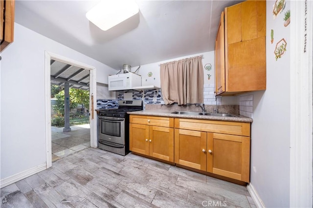 kitchen with a sink, white microwave, gas range, decorative backsplash, and brown cabinetry
